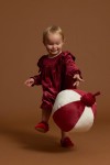Petite fille souriante tenant boule de Noël en robe Idalia velours bordeaux