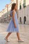 Robe Rina bleu pervenche portée dans une rue de vieille ville – silhouette entière de profil