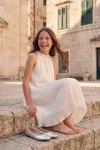 Robe Rozalia blanche plissée en extérieur – assise sur des marches en pierre