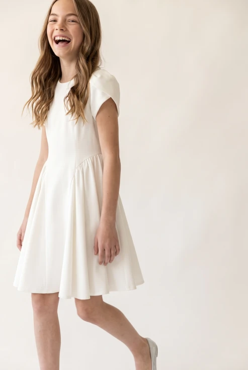 Robe de communion Rumi blanche à manches tulipe – enfant souriante en mouvement, vue de face